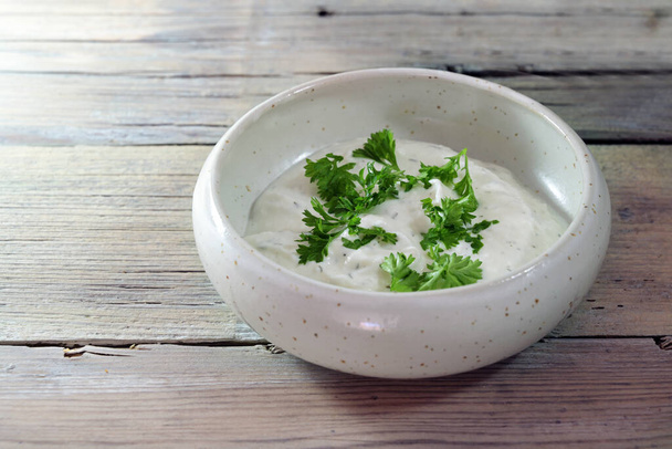 Yogurt dip with herbs and parsley garnish in a small ceramic bowl on a light rustic wooden table, copy space, selected focus, narrow depth of field - Foto, imagen