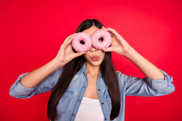 Portrait of attractive crazy girl holding muffin like glasses grimacing pout lips having fun isolated over bright red color background - Fotó, kép