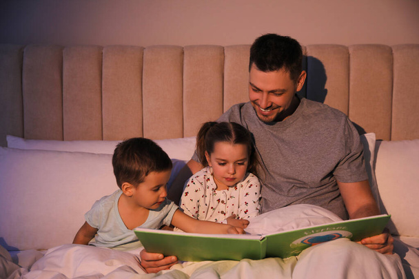 Father reading bedtime story to his children at home - Foto, afbeelding