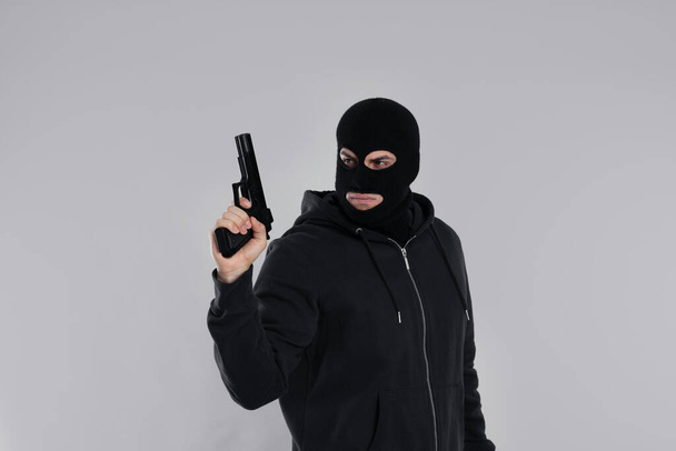 Man wearing black balaclava with gun on light grey background - Photo, image