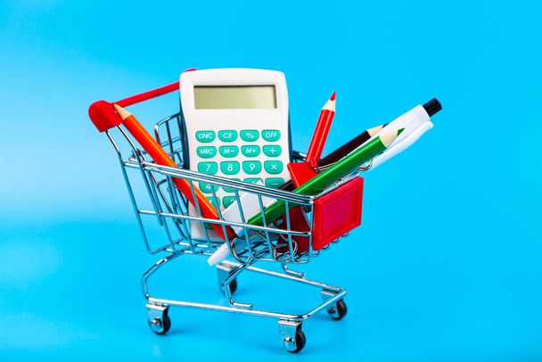 Stationery and shopping cart on a blue background. Shopping for school. Back to school. - 写真・画像