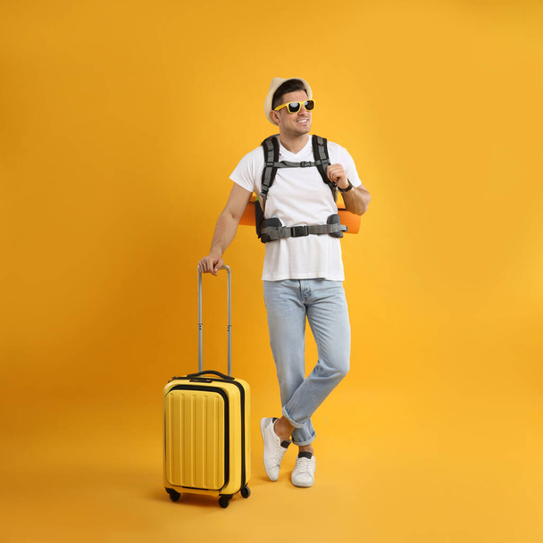 Male tourist with travel backpack and suitcase on yellow background - Photo, image