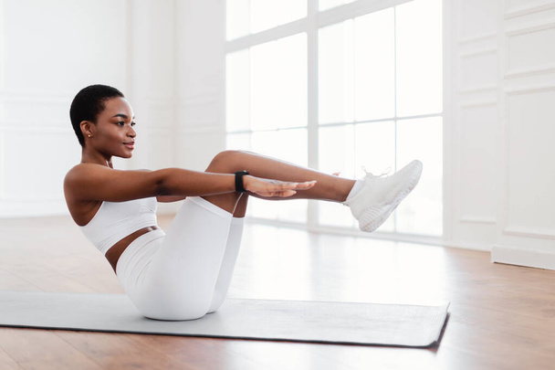 Yoga minderi üzerinde Crunches egzersizi yapan odaklanmış siyah bir kadın. - Fotoğraf, Görsel