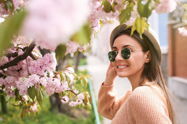 Happy stylish young woman near blossoming sakura tree outdoors. Spring look - Foto, Imagem