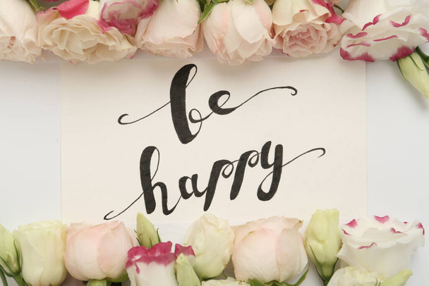 Frame of beautiful flowers and paper card with handwritten text Be happy on white background, flat lay - 写真・画像