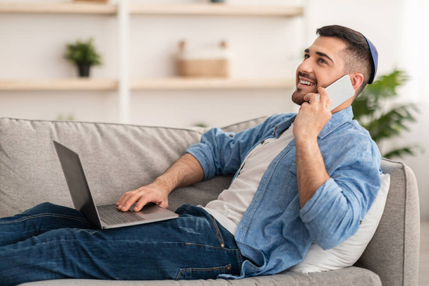Tipo judío usando la computadora y hablando por teléfono celular en casa - Foto, Imagen