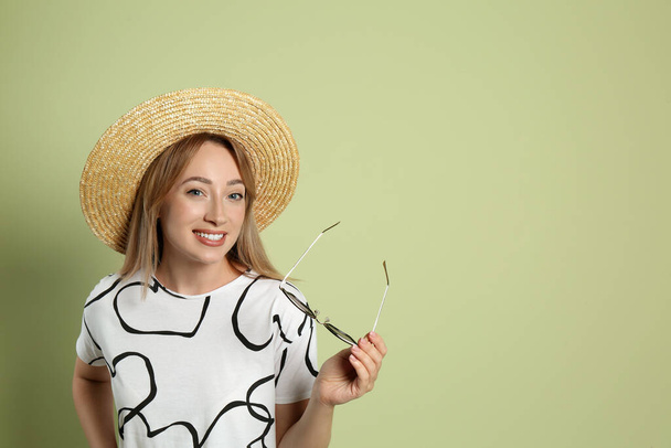 Beautiful young woman with straw hat and sunglasses on light green background, space for text. Stylish headdress - Фото, изображение