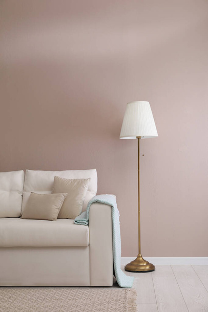 Stylish room living interior with comfortable sofa and lamp near beige wall - Foto, afbeelding