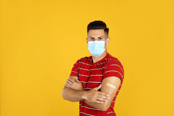 Vaccinated man with protective mask and medical plaster on his arm against yellow background - Foto, afbeelding