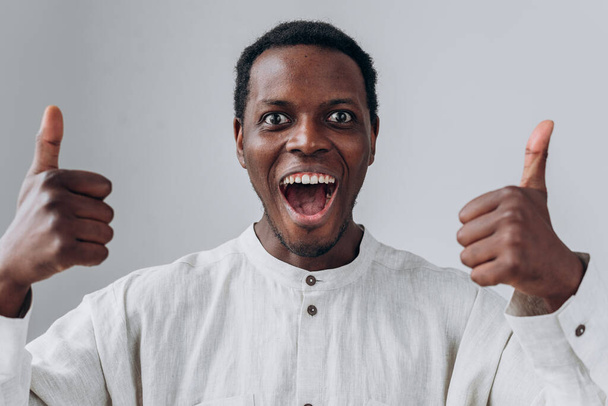 Emocjonalny Afroamerykanin pokazuje kciuki do góry na jasnoszarym - Zdjęcie, obraz