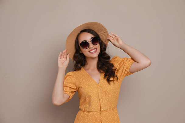 Beautiful young woman with straw hat and stylish sunglasses on beige background - Foto, imagen