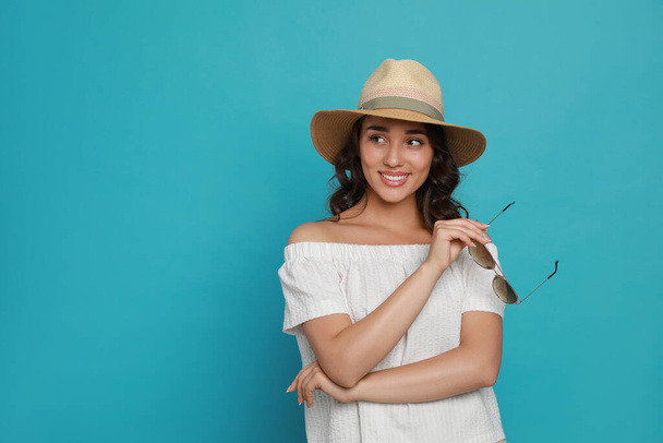 Beautiful young woman with straw hat and stylish sunglasses on light blue background. Space for text - Фото, изображение