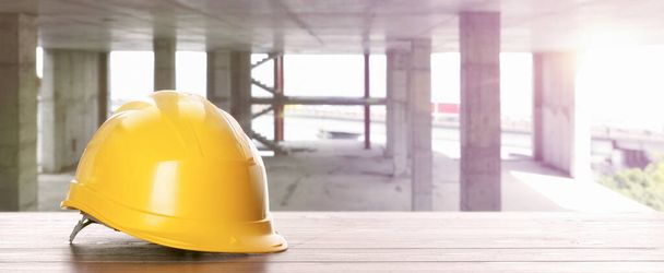 Hard hat on white wooden surface at construction site with unfinished building, banner design. Space for text  - Photo, image