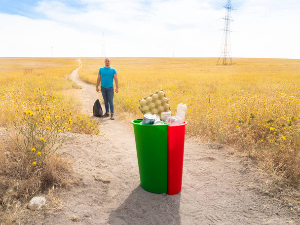Blanke man recycling van afval en afval in het gele bos met rode en zwarte groene recycling bakken met plastic aluminium en karton - Foto, afbeelding