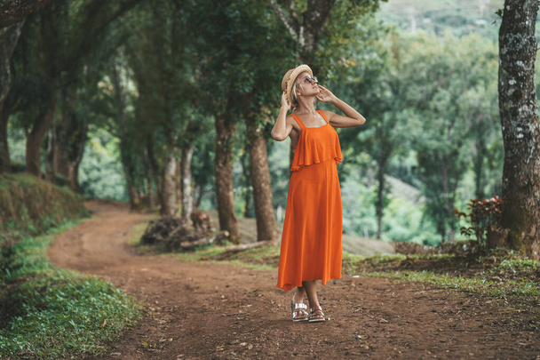 Woman in orange dress is walking by Alley of trees at Tea plantation in mountain, Doi Mae Salong, Chiang Rai, Thailand - Foto, imagen