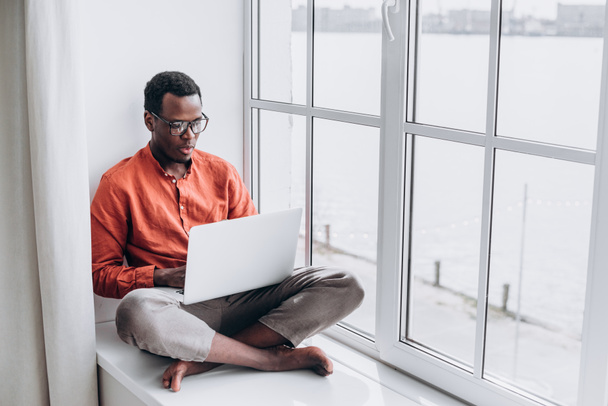 Black man surfs internet on laptop sitting on sill - Foto, Imagem