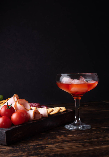 Glas mit rotem Schnaps und Wurstbrett, alkoholischer Cocktail mit Vorspeise, Nahaufnahme. - Foto, Bild