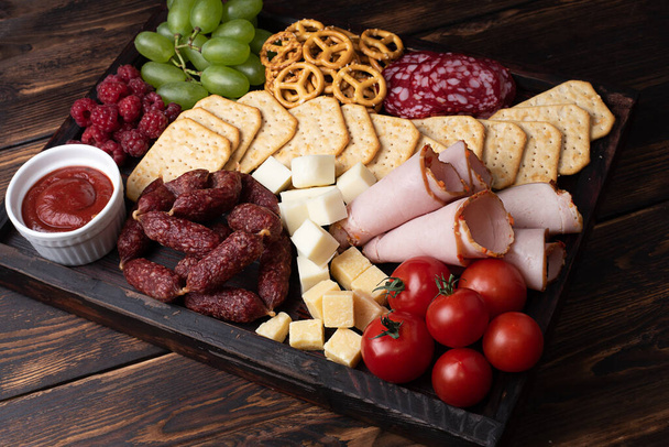 Embutidos, quesos y charcutería de frutas sobre un fondo de madera oscura, aperitivos para fiestas, primer plano. - Foto, Imagen