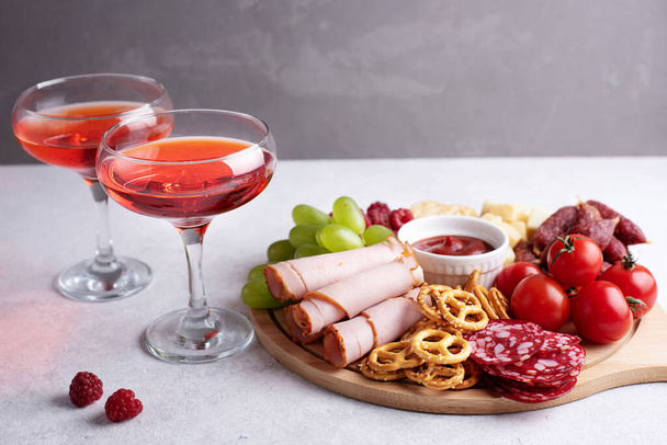 Two glasses with red liquor and round charcuterie board with various snacks on a gray background, party a appetizer, close-up. - Photo, Image