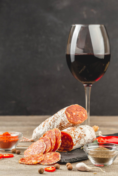 Нарезанная колбаса Чоризо с бокалом красного вина, вертикальная композиция с копировальным пространством - Фото, изображение