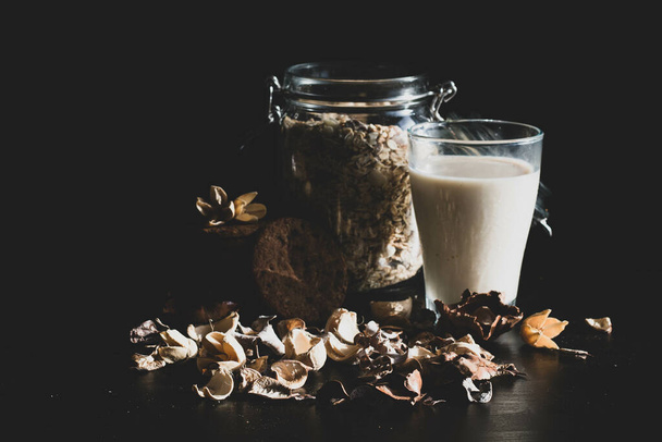 A glass of oat milk, a jar filled with whole oat grains and cookies on a black background - Fotoğraf, Görsel