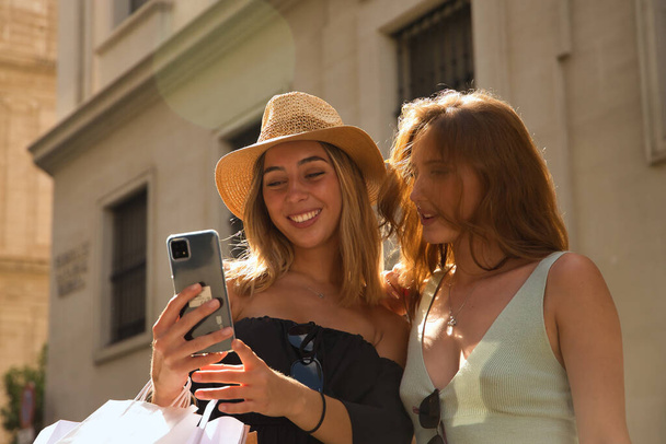 Portrét dvou mladých žen, jak se dívají na mobil jedné z nich, jak se smějí. - Fotografie, Obrázek