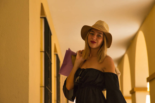帽子の若い女性の肖像画と黒のドレスで彼女の背中にショッピングバッグ. - 写真・画像