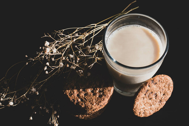 A glass of oat milk and oat cookies on a black background - Zdjęcie, obraz