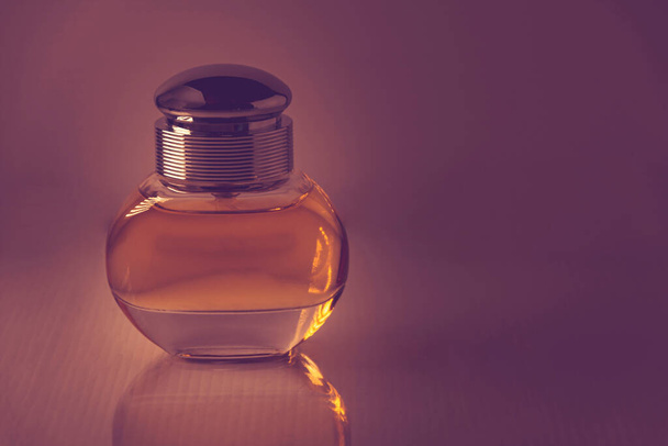 A closeup shot of a perfume on a dark purple background - Фото, зображення