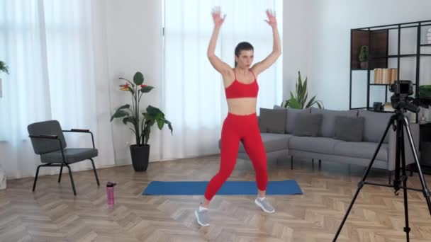 Підходить красива жінка фітнес-тренер блогер робить стрибки вправи, тренування будинку
 - Кадри, відео