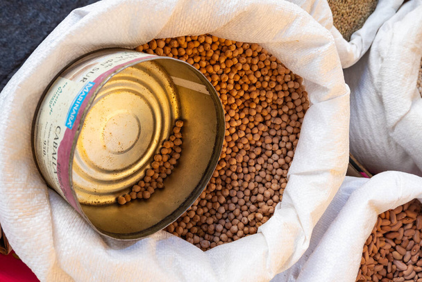 PLASENCIA, SPAIN - Mar 23, 2021: The sale of chickpeas at a street market displayed in a sack and served with an old tin can - Photo, image