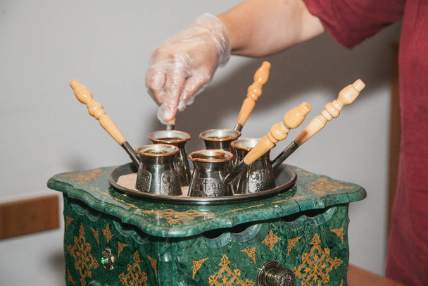 Γυναίκα κάνει τούρκικο καφέ σε μια μηχανή καφέ με άμμο σε cezve. Ανατολικός, ανατολικός καφές. - Φωτογραφία, εικόνα