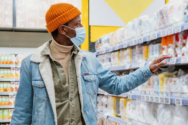 マスクをしたアフリカ系アメリカ人男性はスーパーマーケットで商品を選ぶ - 写真・画像