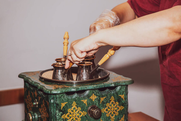 Woman makes turkish coffee on a coffee machine with sand in cezve. Oriental, east coffee. - 写真・画像