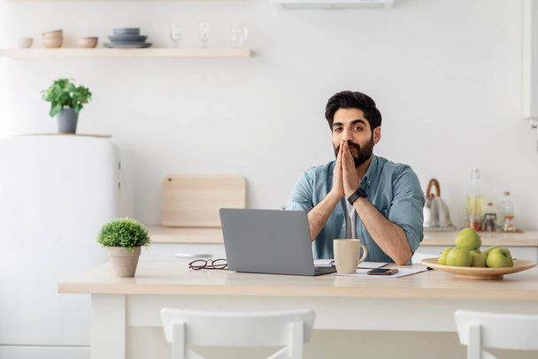 Otthoni kényelmes iroda. Fiatal magabiztos arab férfi munkáltató ül a modern konyha belső laptoppal az asztalon - Fotó, kép