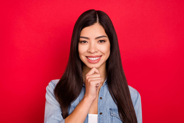 Photo of young cheerful asian girl happy positive smile hand touch chin dream think isolated over red color background - Foto, Imagen
