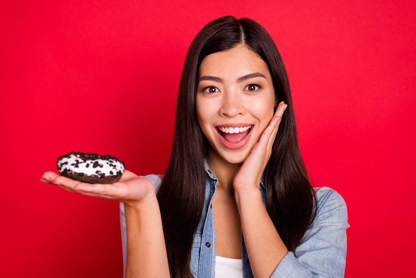 Portrait of attractive impressed girlish cheerful girl holding delicious doughnut having fun isolated over bright red color background - Фото, зображення
