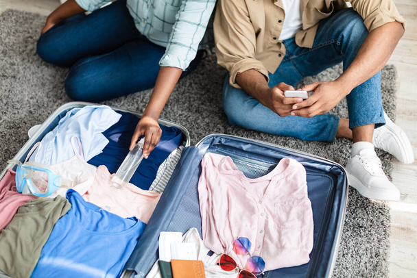 Couple de touristes noirs mettant désinfectant emballage valise de voyage à la maison - Photo, image