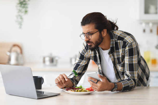 Irritated middle-eastern guy having snack while working from home - Photo, Image