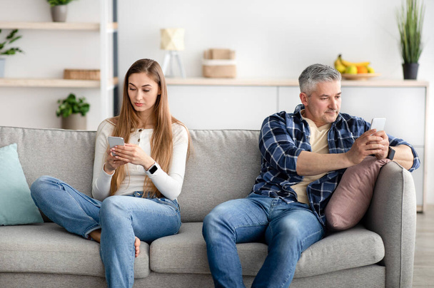 Зріла пара використовує мобільні пристрої, сидячи на дивані, не звертаючи уваги один на одного, граючи в онлайн ігри
 - Фото, зображення