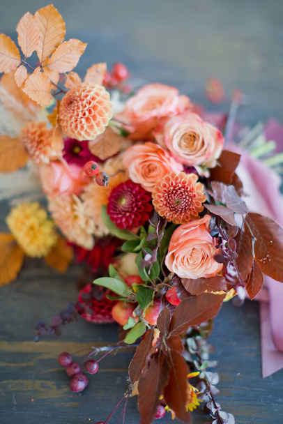Hermoso ramo de otoño con flores y bayas naranjas y rojas. Ramo de otoño con cintas en una mesa de madera - Foto, imagen