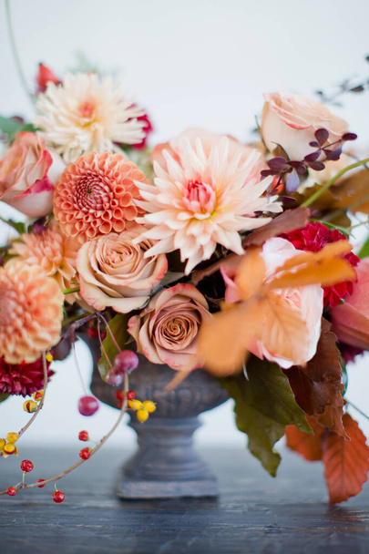 Beautiful flower composition with autumn orange and red flowers and berries. Autumn bouquet in vintage vase on a white wall background - Zdjęcie, obraz