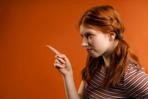 Ginger displeased woman with tails looking and pointing finger aside isolated over orange background - Photo, Image