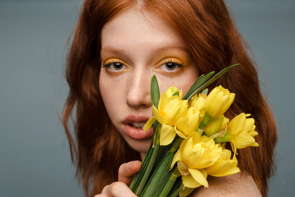 Shirtless ginger white woman posing with yellow flowers isolated over grey background - Foto, immagini