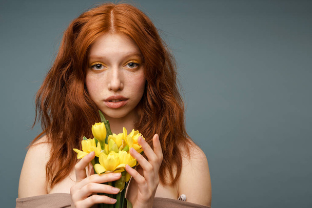 Shirtless ginger white woman posing with yellow flowers isolated over grey background - Foto, Bild