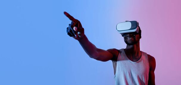 Virtual reality sporten. Millennial zwarte man in VR headset selecteren opties op denkbeeldig scherm in neon licht, banner - Foto, afbeelding