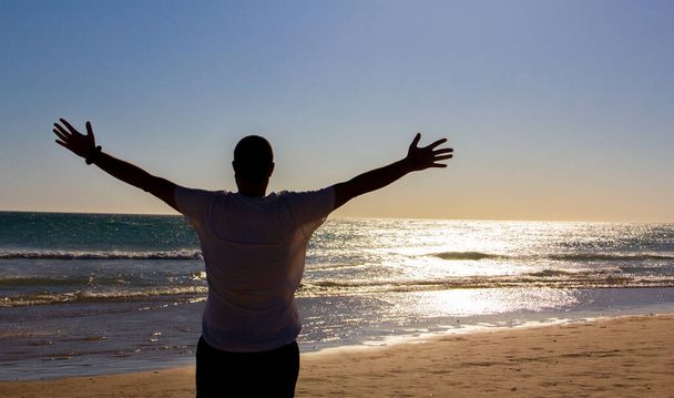 Мальчик с протянутыми руками смотрит на море на закате. Концепция freedom.backlighting. - Фото, изображение