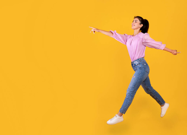Aufgeregte armenische Frau läuft und zeigt Kopierraum über gelbem Studiohintergrund, leerer Raum - Foto, Bild