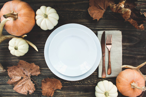 Holiday place setting with plate, napkin, antlers and silverware on a Thanksgiving Day decorated table shot from flat lay or top view position. Pumpkins, antlers and fallen leaves.  - Zdjęcie, obraz