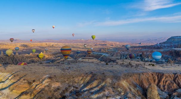 Urgup, Cappadocia, Turkey - March 19, 2021 - beautiful panoramic aerial sunrise view of hot air balloons flying over amazing landscapes with fairy chimney, rock formations, and mountains in Cappadocia - Fotoğraf, Görsel